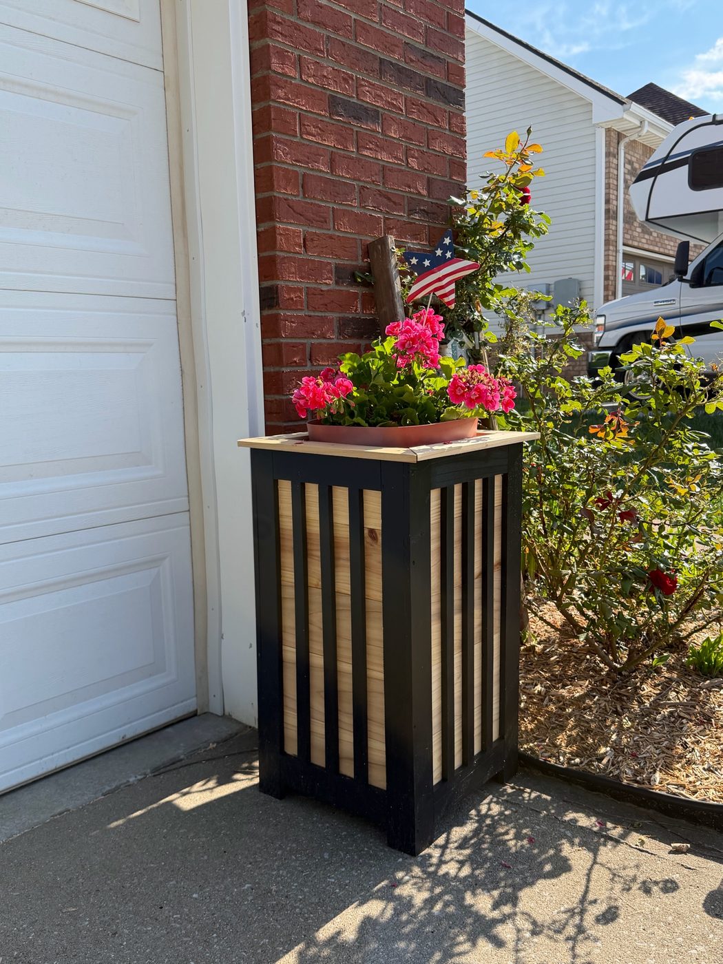 Tall slatted black and cedar planter with flowers at a home entry