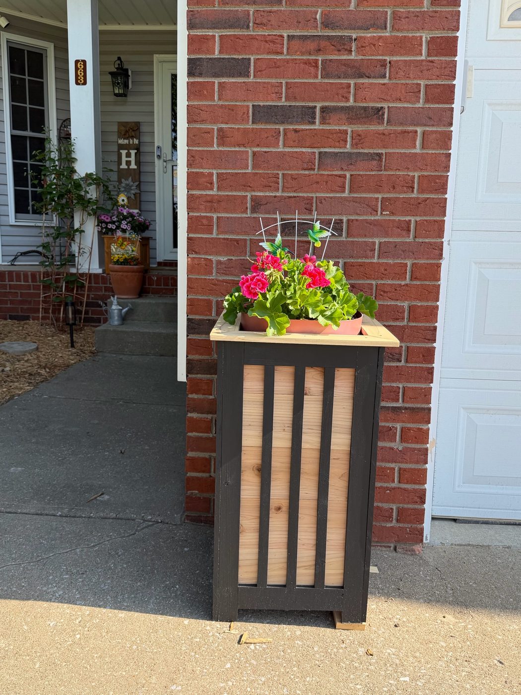 Signature black and cedar slatted planter with red flowers on a brick porch